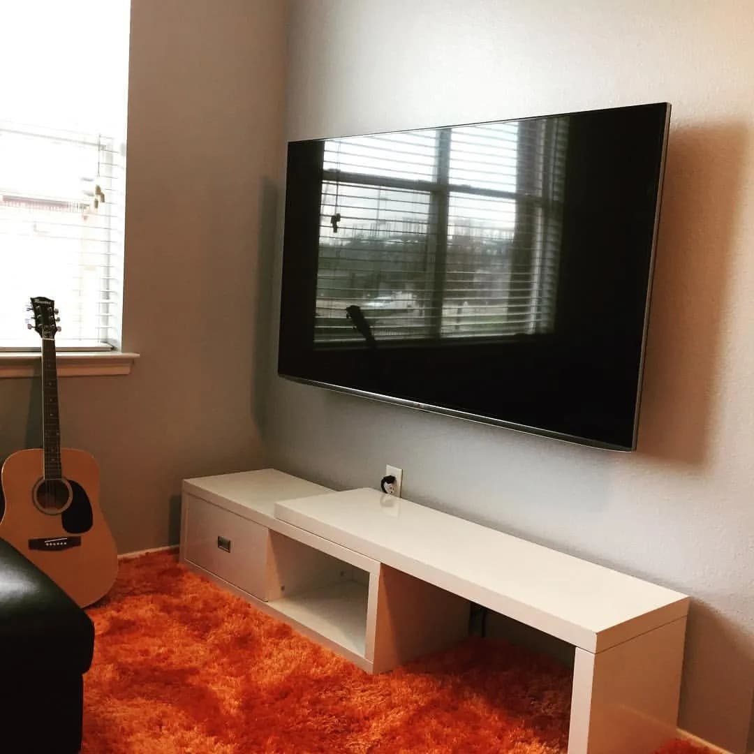 Large TV mounted in living room with orange rug and guitar