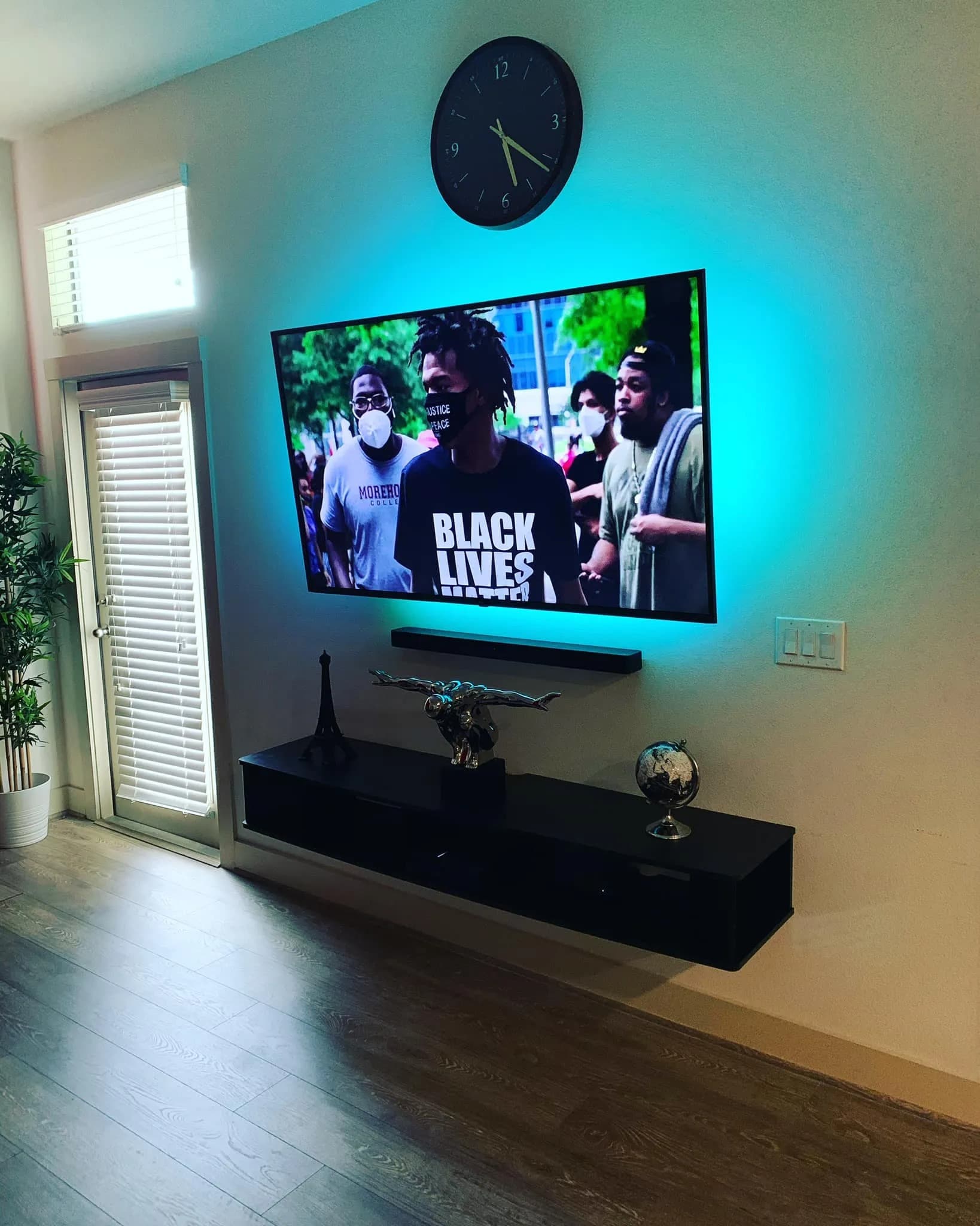 TV with teal LED backlight above floating shelf with plants